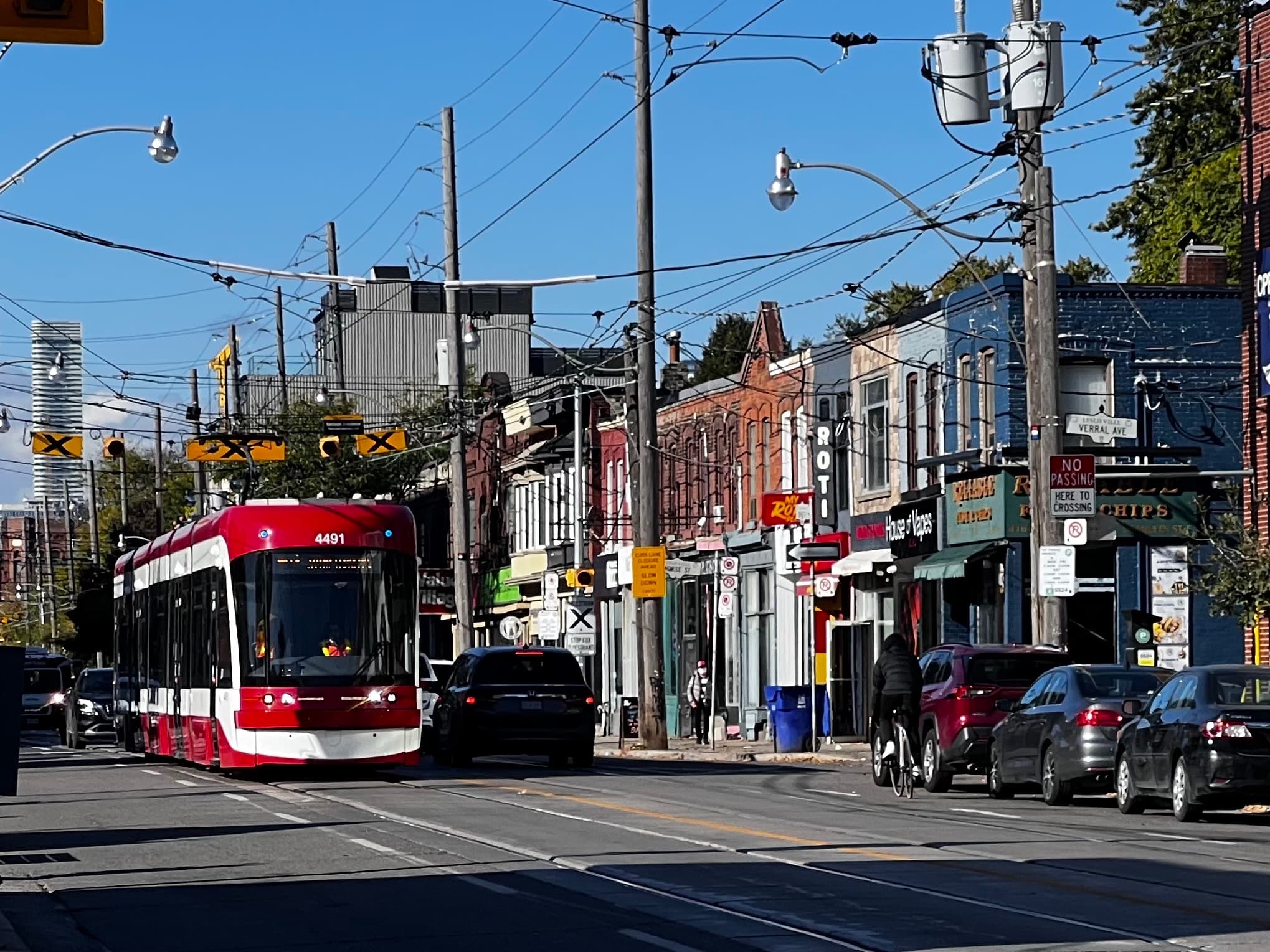 Queen Street East at Verral Avenue, Leslieville, Toronto — TTC streetcar, storefronts, and curb parking along the strip